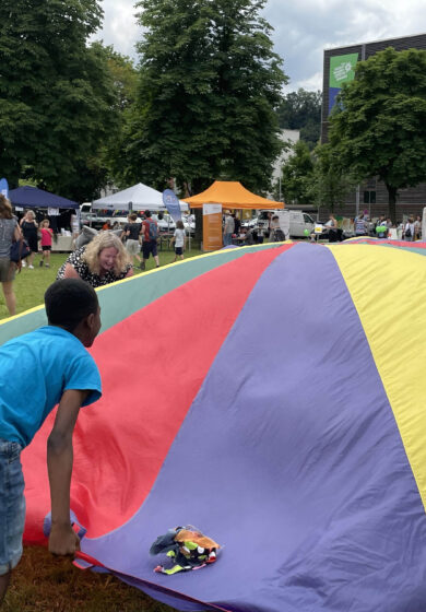 Kinder und Mitarbeiter mit einem großen Tuch lachend auf der Wiese der Alten Kaserne beim Familienfest